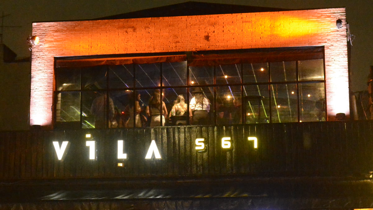 Fachada do Vila 567 à noite, com o letreiro aceso e o janelão do rooftop