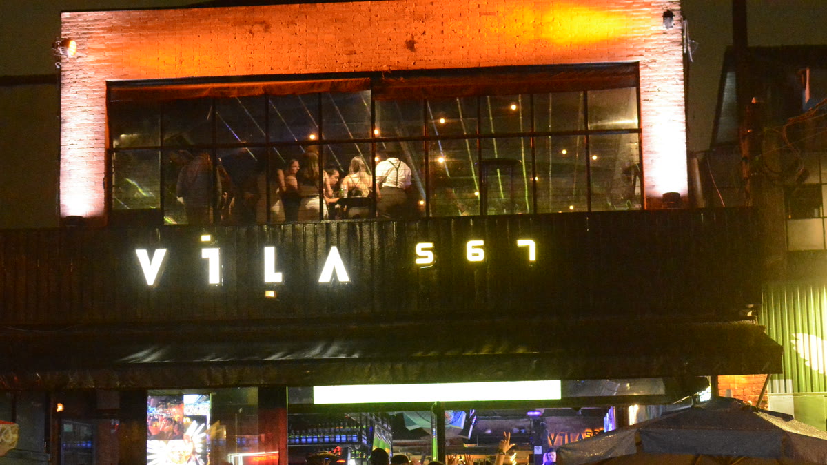 Fachada do Vila 567 à noite, com o janelão aceso e o letreiro VILA 567