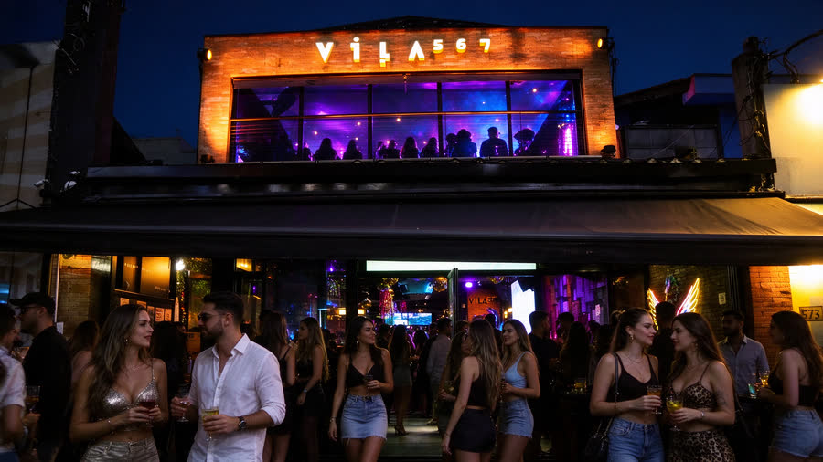 Fachada do Vila 567 à noite com o letreiro aceso e gente chegando